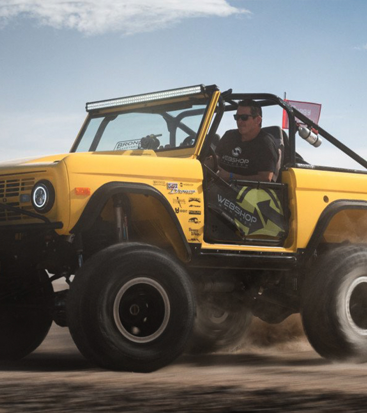 The owner driving his yellow bronco in the desert.